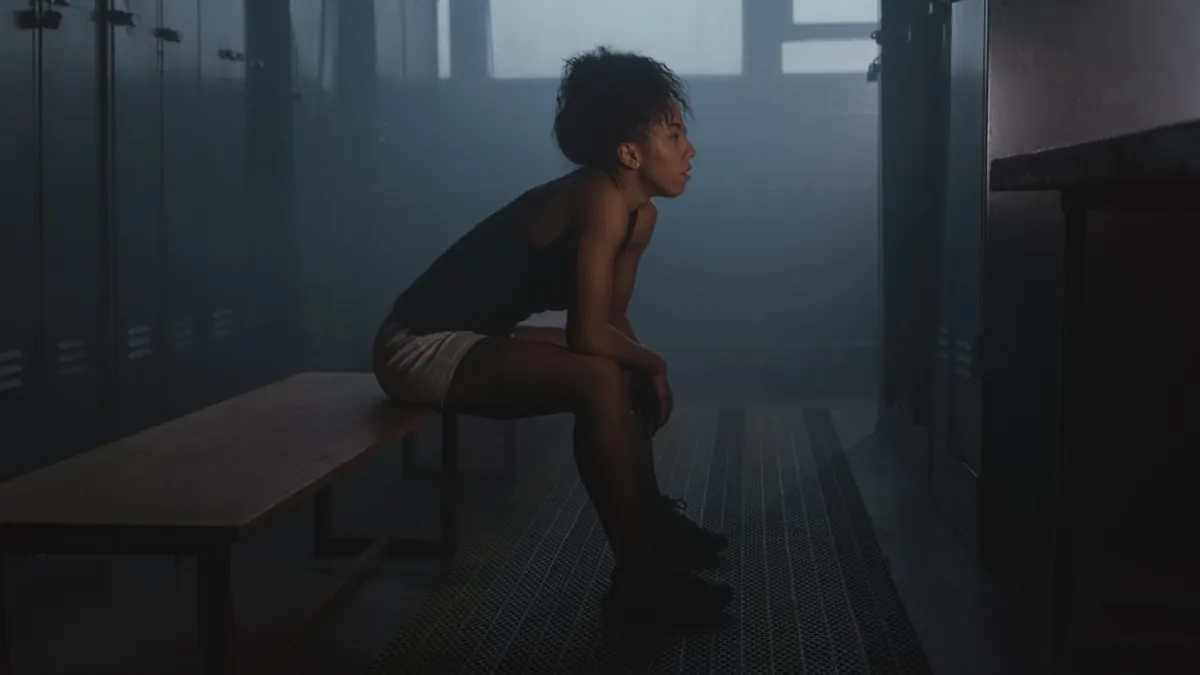 Sportive assise seule dans un vestiaire sombre, le regard fixe avant une compétition