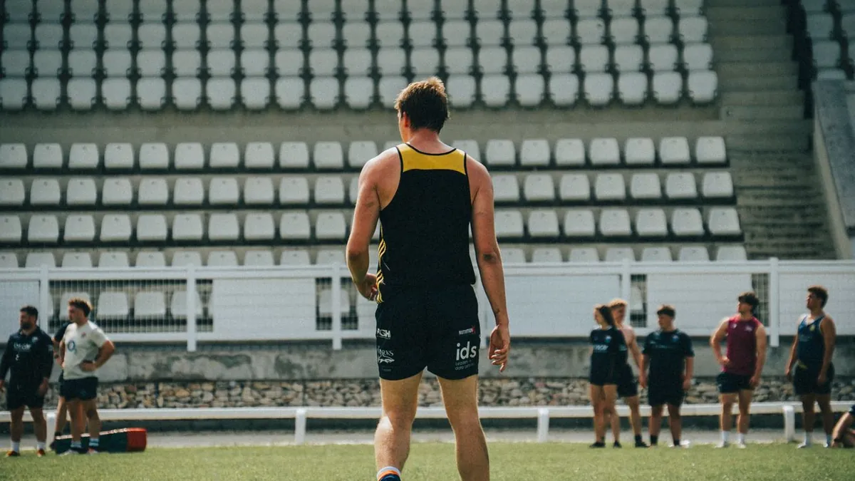 Joueur de rugby de dos sur un terrain, face à ses coéquipiers et à des gradins vides