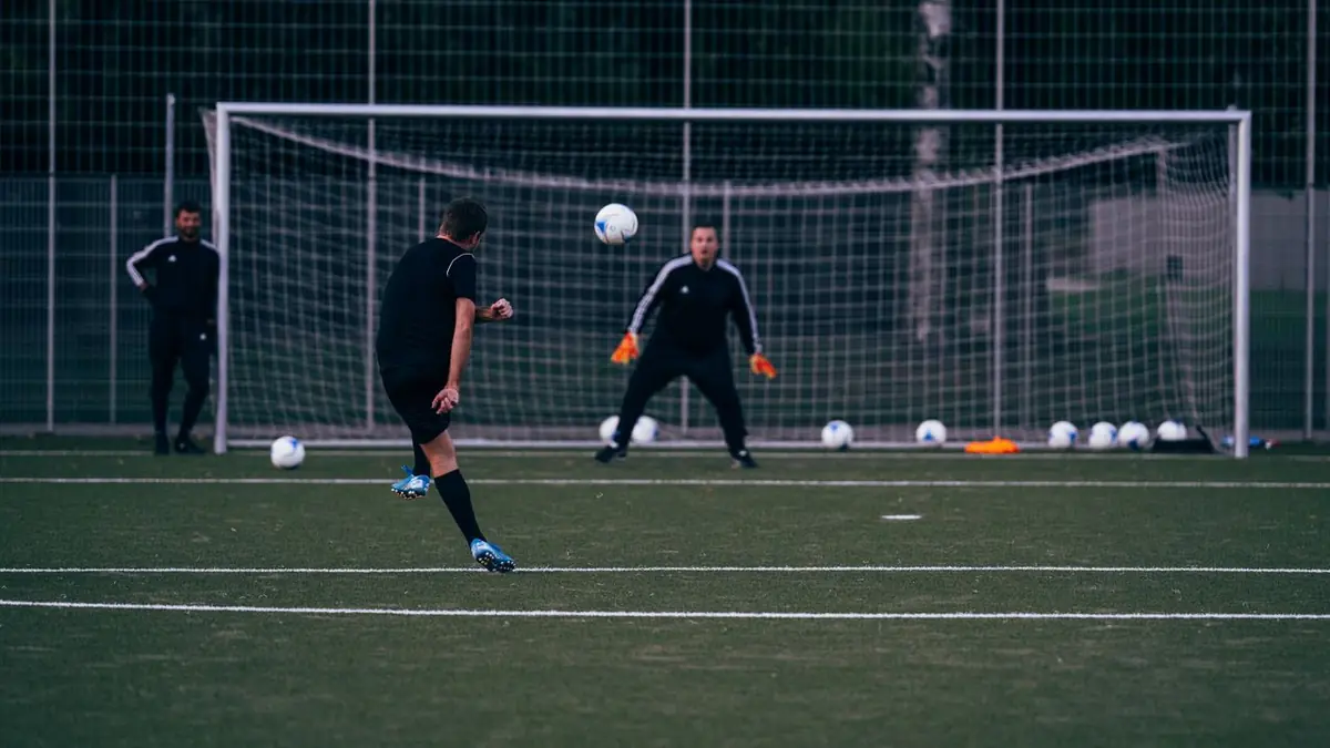 Joueur de football qui tire au but face à un gardien lors d'un entraînement