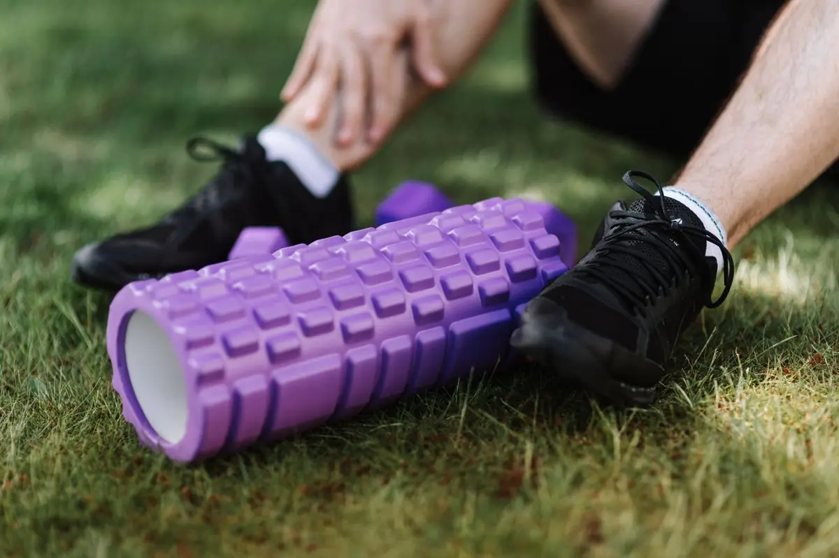 Sportif assis dans l'herbe avec un foam roller, en récupération après un effort