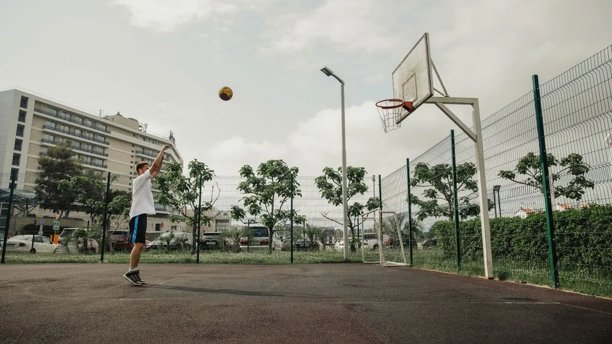 Joueur de basket qui vient de lancer le ballon vers le panier sur un terrain extérieur